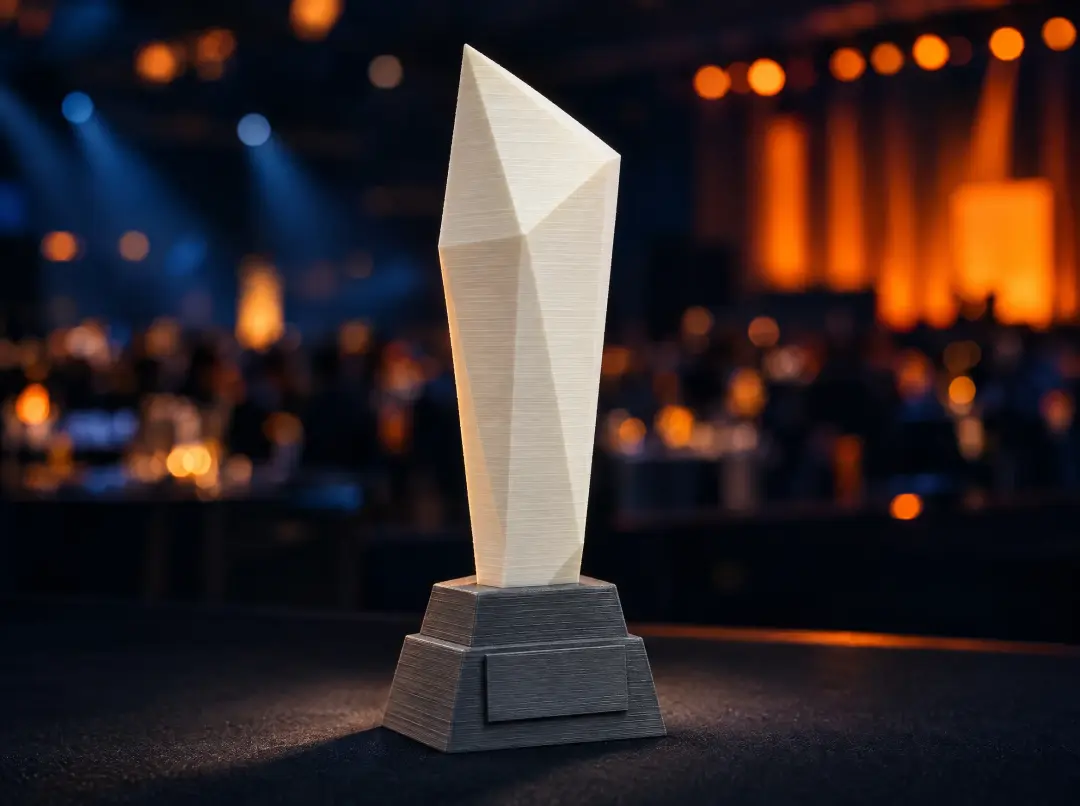 Troféu facetado em PLA branco sobre base grafite impressa, num palco de premiação